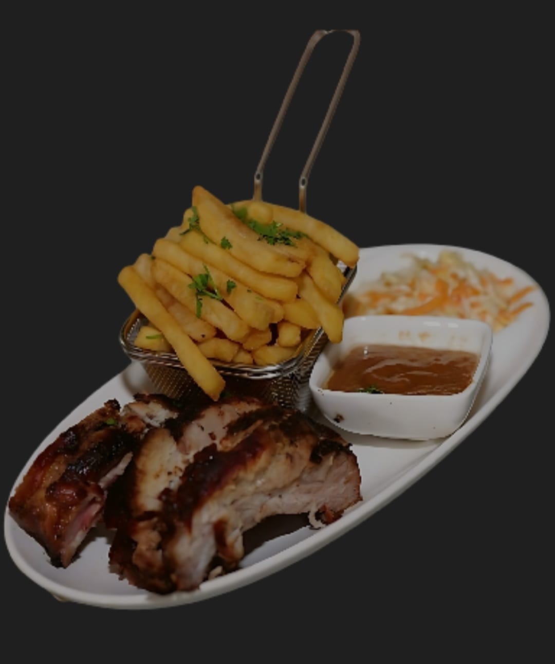 Grilled ribs on an oval plate with fries, coleslaw and sauce